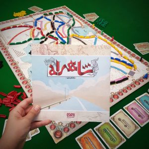بازی رومیزی شاهراه، دفترچه راهنما در دست بچه و صفحه بازی روی میز